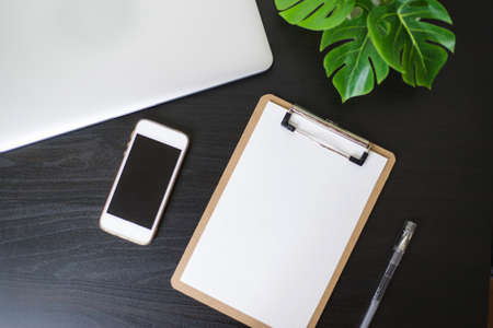 Still life, business, office supplies or education concept : Top view image of open notebook, clip board with blank pages and laptope and pen and phone and flower on wooden dark background, ready for adding or mock upの写真素材