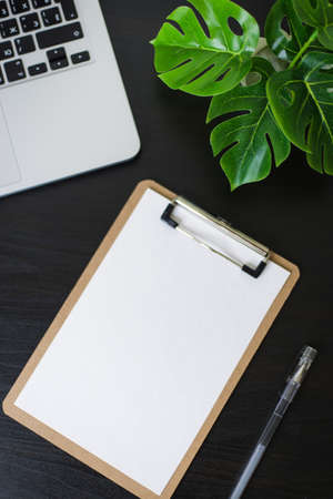 Still life, business, office supplies or education concept : Top view image of open notebook, clip board with blank pages and laptope and pen and phone and flower on wooden dark background, ready for adding or mock upの写真素材