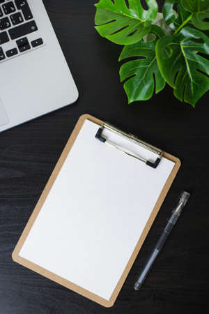Still life, business, office supplies or education concept : Top view image of open notebook, clip board with blank pages and laptope and pen and phone and flower on wooden dark background, ready for adding or mock upの写真素材