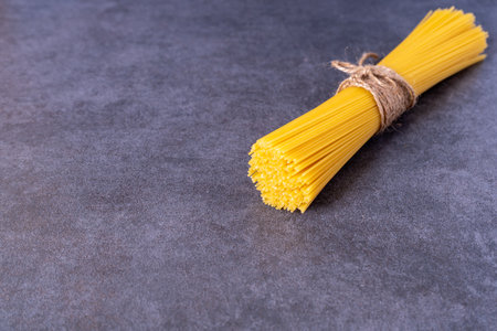 Cooking Italian pasta concept. A bunch of raw yellow spaghetti isolated on dark grey stone background with copy space. Long thin uncooked whole wheat pieces of macaroni in top right corner.の写真素材