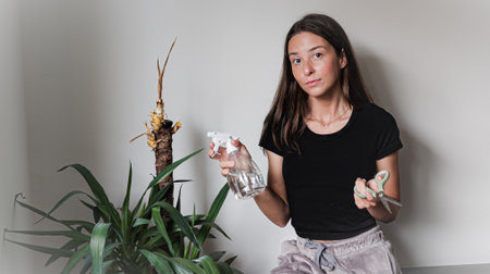 Young woman caring for houseplant at home, confused about dried palm leavesの写真素材