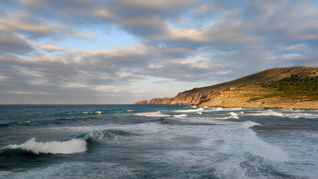 Horizontal seascape with stormy waves, green mountains and cloudy skyの写真素材