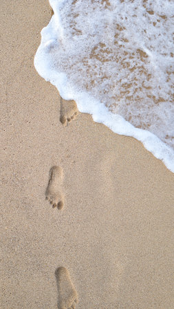 Footprints on Wet Yellow Sand with Gentle Waveの写真素材