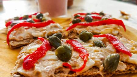 Pizza with cheese, tomatoes and capers on a wooden board