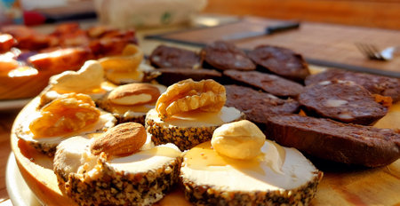 Slices of cheese, meat and nuts on a wooden board.