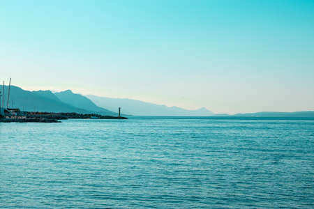 Bright blue morning sunrise on the shore of split, lighthouse in the distance with mountain silhouettes going into the distanceの写真素材