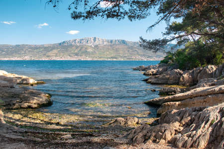 Small hidden beach in a cove on Marjan hill in Split, Croatia. Beautiful sea in the shade, mountains and coastal towns seen in the distanceの写真素材