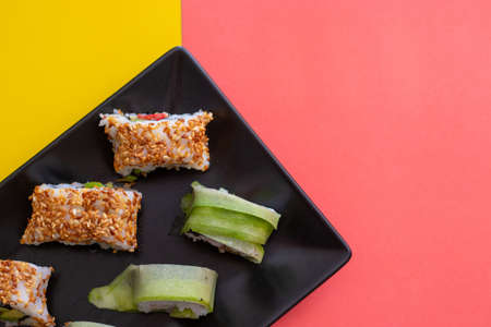 Top down closeup view of a sushi plate with sesame seeds and cucumber wrap on a combination of vibrant pink and yellow colors. Right area left for copyspaceの写真素材