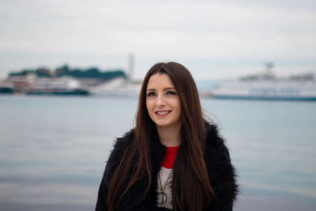 Attractive brunette in a black furry coat posing on a summer day with blue adriatic sea and ferries in the distance. Town of Split, Croatiaの写真素材