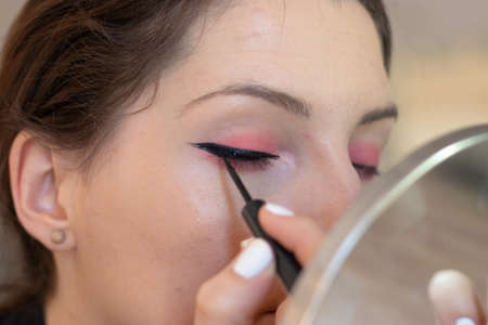 Closeup of an adult brunette aplying eye liner on herself, eyes closed while creating cat eyes