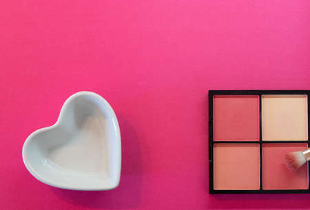 White ceramic heart shaped plate and a make up box on a pink backgroundの写真素材
