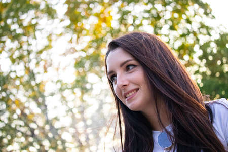 Young brunette smiling looking into the distance , green white background bokeh on a warm summer day.の写真素材