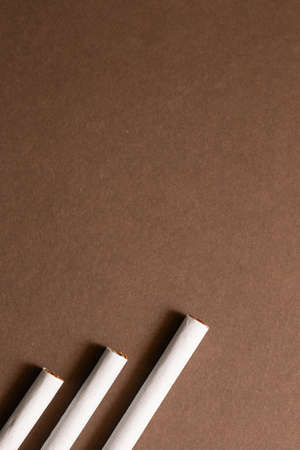 Three cigarettes poking from below on a brown background. Above area left for copyspaceの写真素材