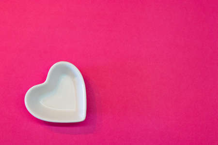 White ceramic heart shaped plate on a simple pink background from aboveの写真素材
