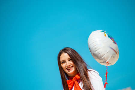 Happy brunette student in white business casual outfit holding a baloon celebrating a graduation. Happy sunny dayの写真素材