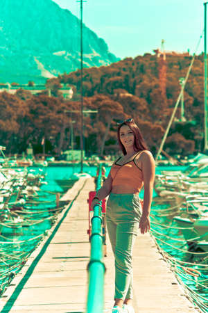 Brunette red haired woman with tank top and grey pants posing in a marina in summer. Retro vintage lookの写真素材