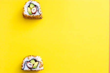 Homemade two pieces of homemade sushi roll above each other. Isolated on yellow background. Avocado, surimi and cucumber with fried sesame seeds, california rollの写真素材