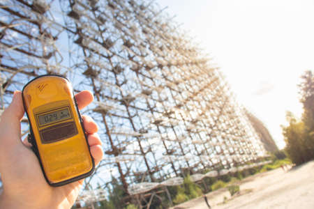 Hand holding a yellow dosimeter indicating radiation on the screen. Enormous Duga radar complex seen...