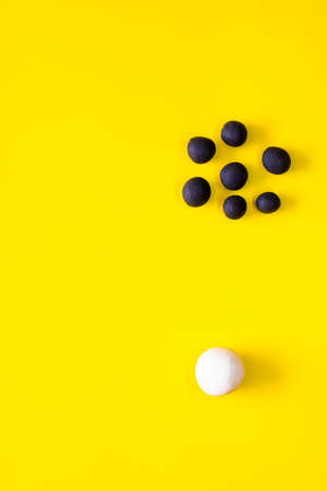One big white ball and many black smaller plasticine balls in a group. Concepts of race and racism. White power and privilege. Area left for copyspace on yellow backgroundの写真素材