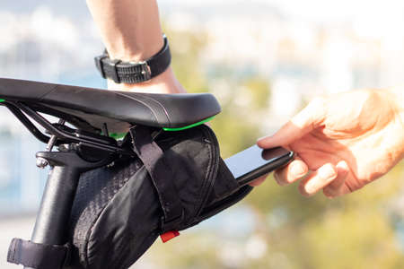 Man putting his smartphone inside a small black pouch for storage under the seat of a bicycleの写真素材