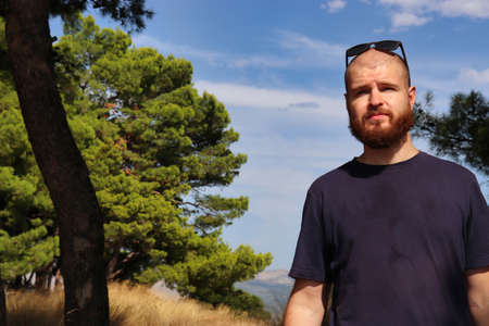 Young bearded bald adult with sunglasses on his head standing outside in nature with a worried...