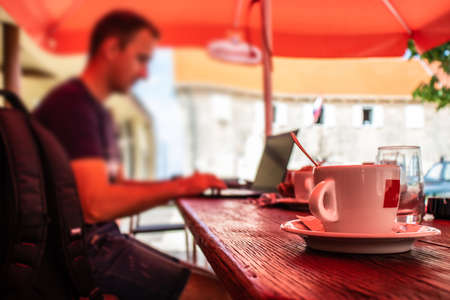 Closeup of a cup of coffee at a dalmatian coffee shop, blurred man sitting on a laptop working,...