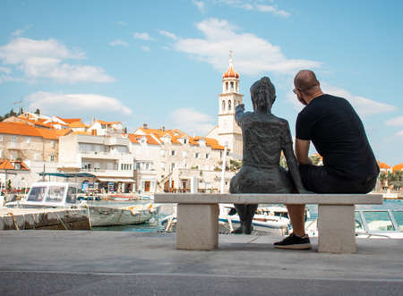 Statue of a little girl pointing at the belltower in a small village of Sutivan in Croatia. Man sitting next to the girl and following her handのeditorial素材