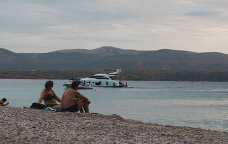 Bol Croatia, August 2020 Elderly couple sitting down on the stones on the beach in a late afternoon...