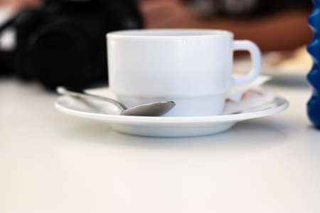 White wide ceramic old fashioned coffee mug standing a white plate with a metal spoon on it