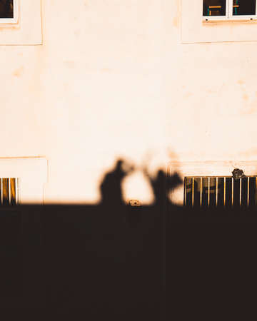 Outlines, sihouettes as shadows are cast on a stone house of two people standing together. One...