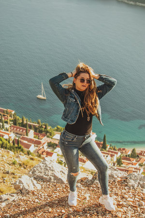 Vertical shot of an attractive brunette with sunglasses posing sensually on a hill above the city of Dubrovnik. Bright blue adriatic sea in the background, warm autumn day in the mediterraneanの写真素材