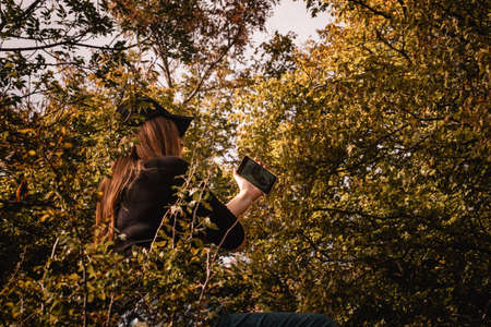 Back view of a brunette wearing a black cap and a black shirt sitting between the leaves in a forest...