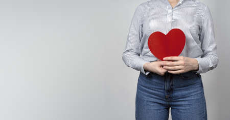 Young woman holding red heart in hands. Symbols: Love and relationships, medicine and heart disease...