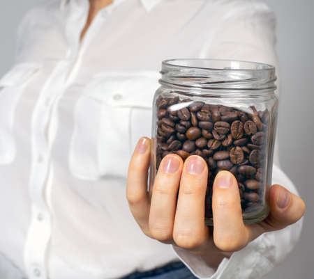 A girl in a white shirt and holds in her hand a glass jar with coffee beans. Square picture.の写真素材
