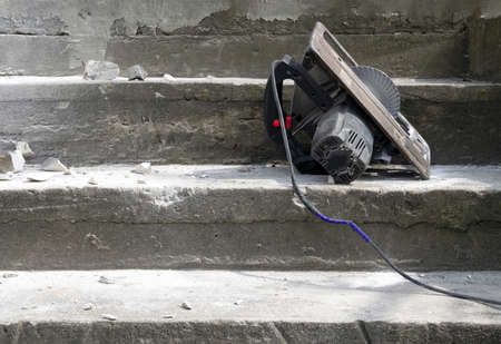 old hand saw on concrete steps, its electrical wire repaired with electrical tape