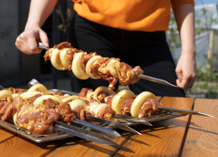 a piece of meat for barbecue on a skewer in the hands of a blurry girl, selective focusの写真素材