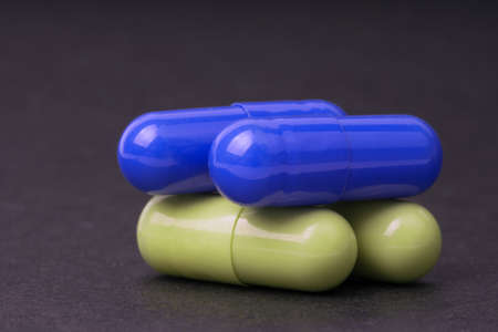 Blue and yellow pills on black background, close up