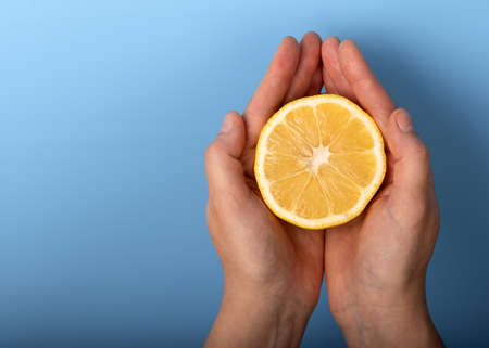 Cut half of a lemon in female hands on a blue background.の写真素材
