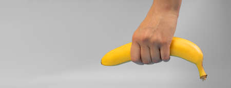 ripe banana in a female hand on a gray background.