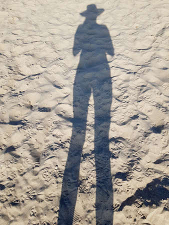shadow of a man with a hat on the beach sand.の写真素材