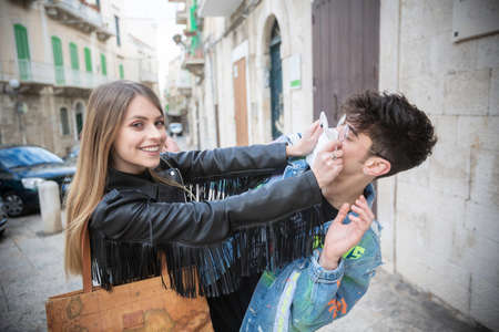 An Italian woman and a young man have fun covering their faces with handkerchiefs to protect themselves from the covid19 virus in the narrow streets of the historic center of the city of Molfettaの写真素材