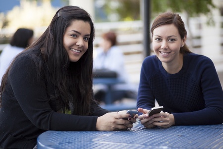 Pretty female students exchanging phone numbers at schoolの写真素材