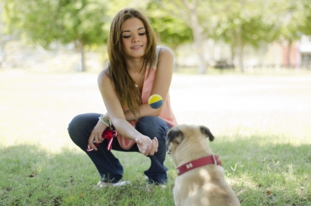 Young beautiful woman and her pug dog playing with a ball at a parkの写真素材