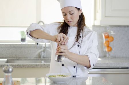 Cute female chef adding some pepper and condiments to a dishの写真素材