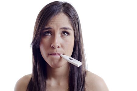 Cute young woman feeling sick and checking her temperature with a thermometerの写真素材