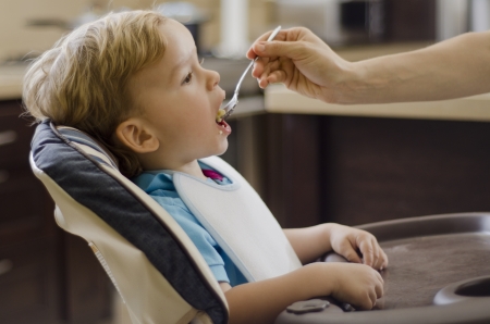 Cute kid being fed with a spoon in the kitchenの写真素材