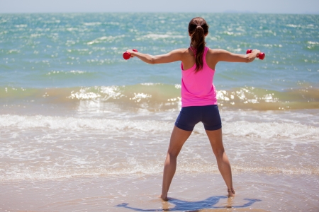 Athletic young woman lifting a couple of dumbbells at the beachの写真素材