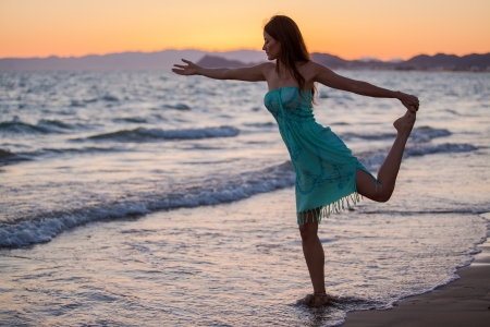 Pretty Hispanic young woman doing a yoga pose at the beach during sunsetの写真素材