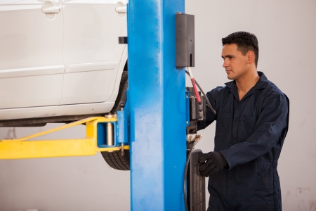 Handsome young mechanic operating a car lift to raise up a car before fixing it at an auto shopの写真素材