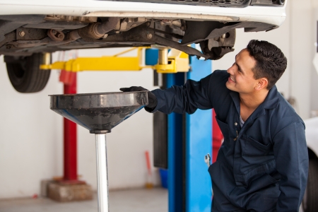 Happy young mechanic changing the oil of a car at an auto shopの写真素材